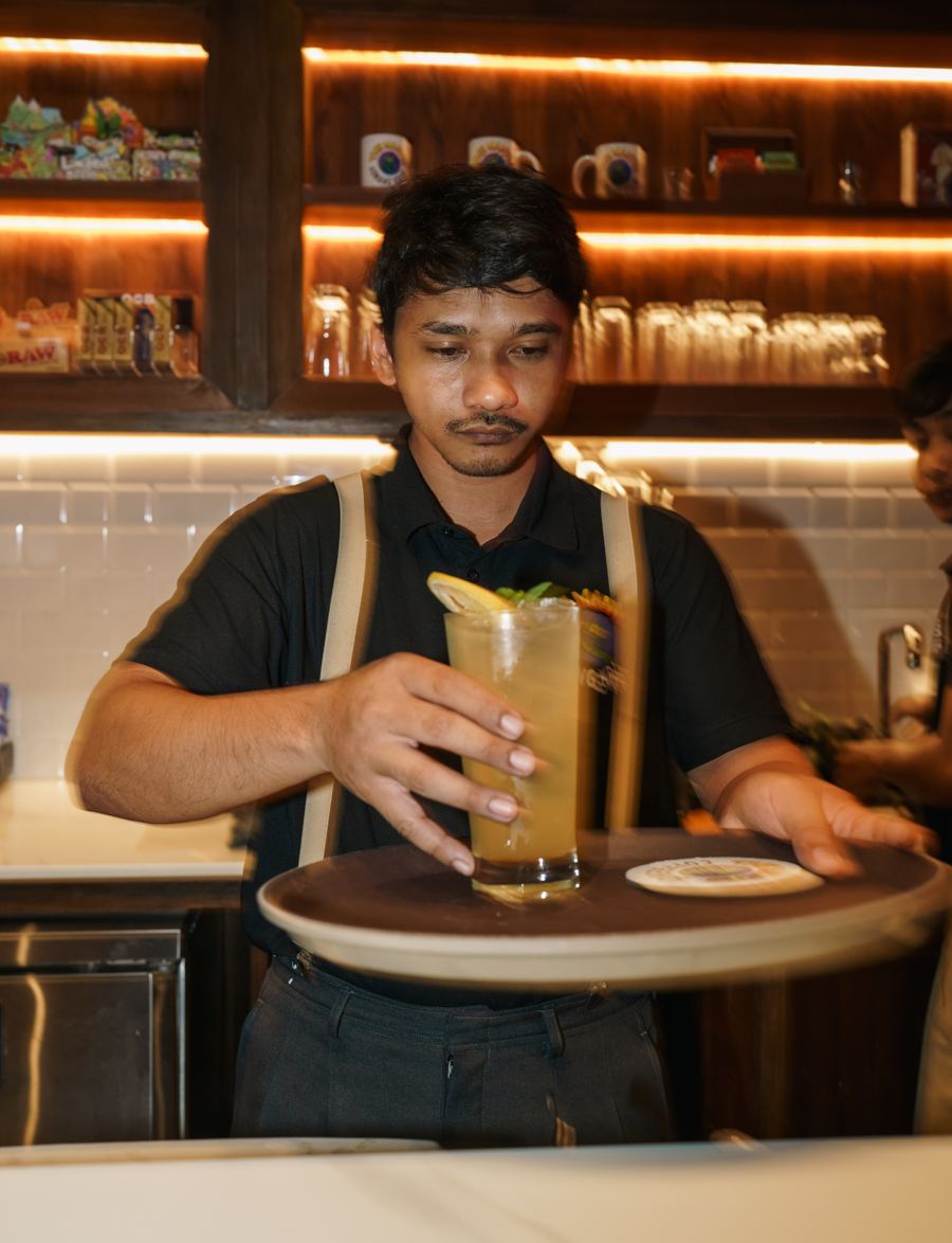 Staff member serving a tall iced drink with lime and mint on a tray